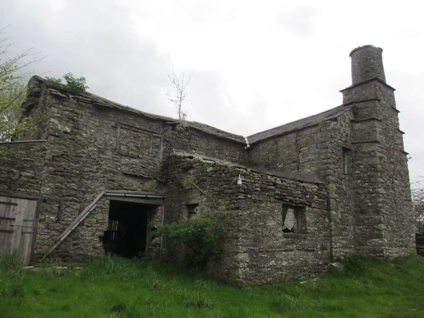 High Hall, the old stone farmhouse in Dent Dale, a derelict building with a chimney, open doorway, and broken windows on a grassy hillside